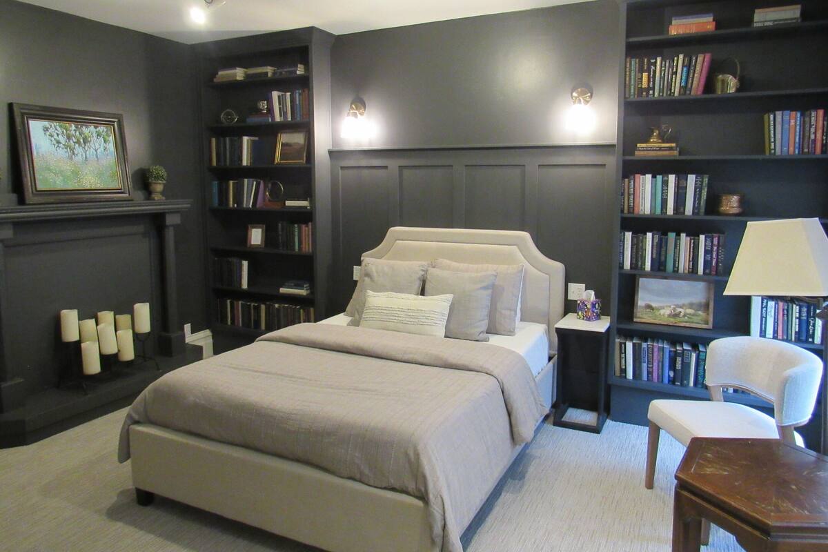 A bedroom with a large bed, a bookshelf, a chair, and a desk.