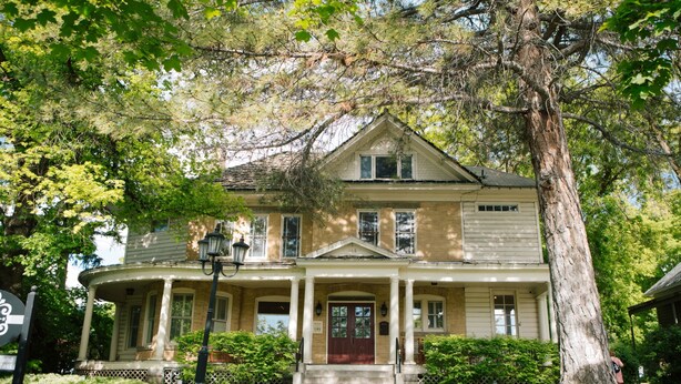 A two-story house with a porch, a large tree in front, and a well-maintained lawn. - The Riter Mansion (Logan)