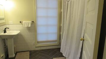 A bathroom with a white sink, a window with blinds, a shower curtain, and a door.