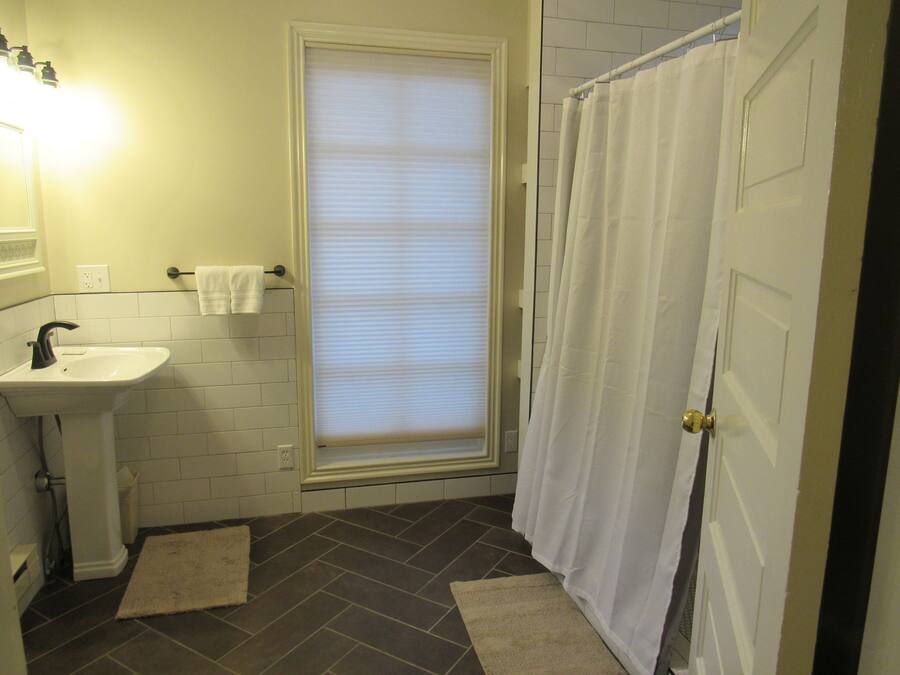 A bathroom with a white sink, a window with blinds, a shower curtain, and a door.