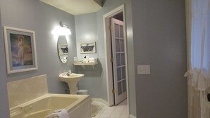 A bathroom with a bathtub, sink, and a door leading to another room. - The Riter Mansion (Logan)