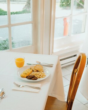 A breakfast table with a plate of food, a glass of orange juice, and cutlery.