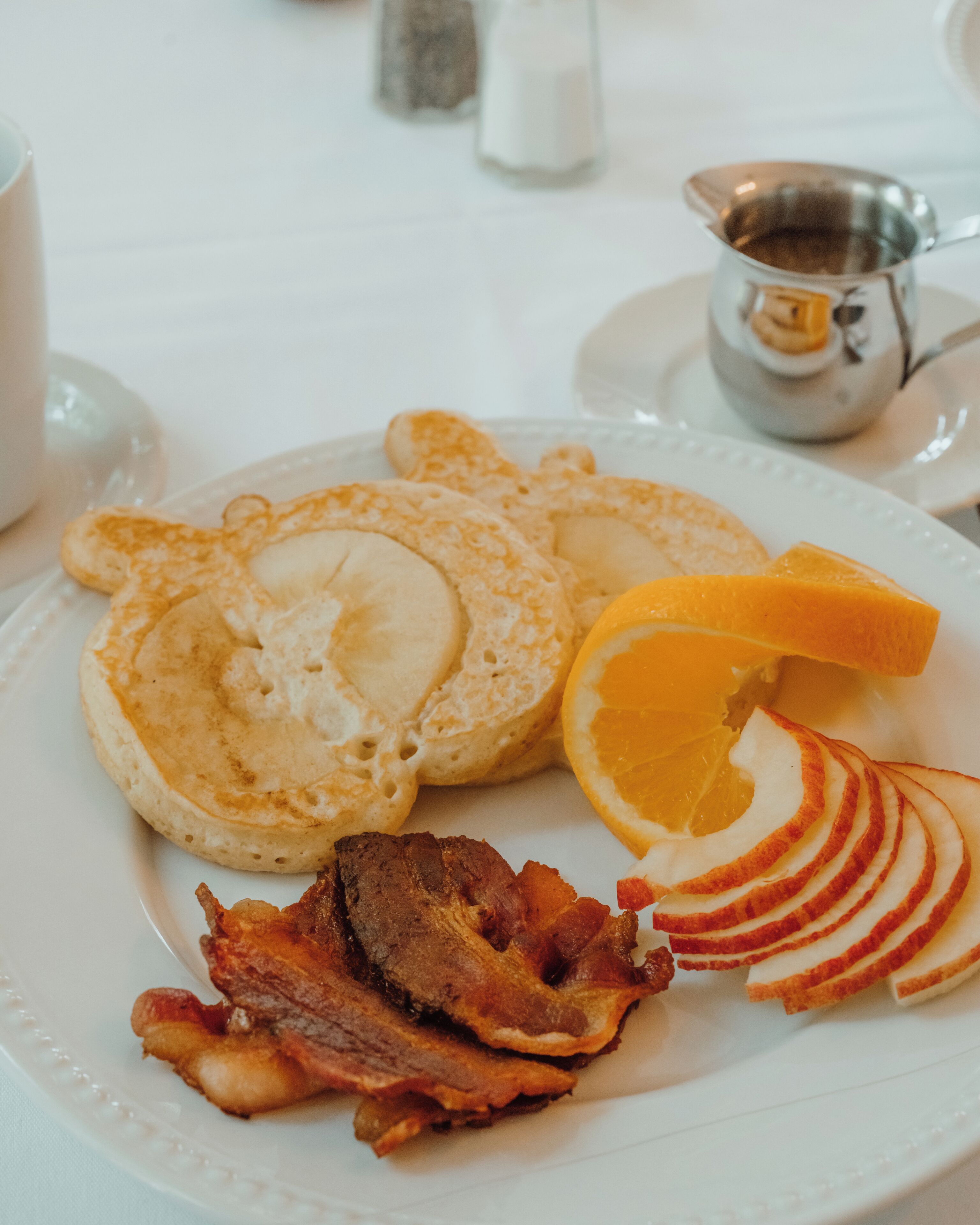 Un plato de desayuno con tortitas, tocino y rodajas de manzana.