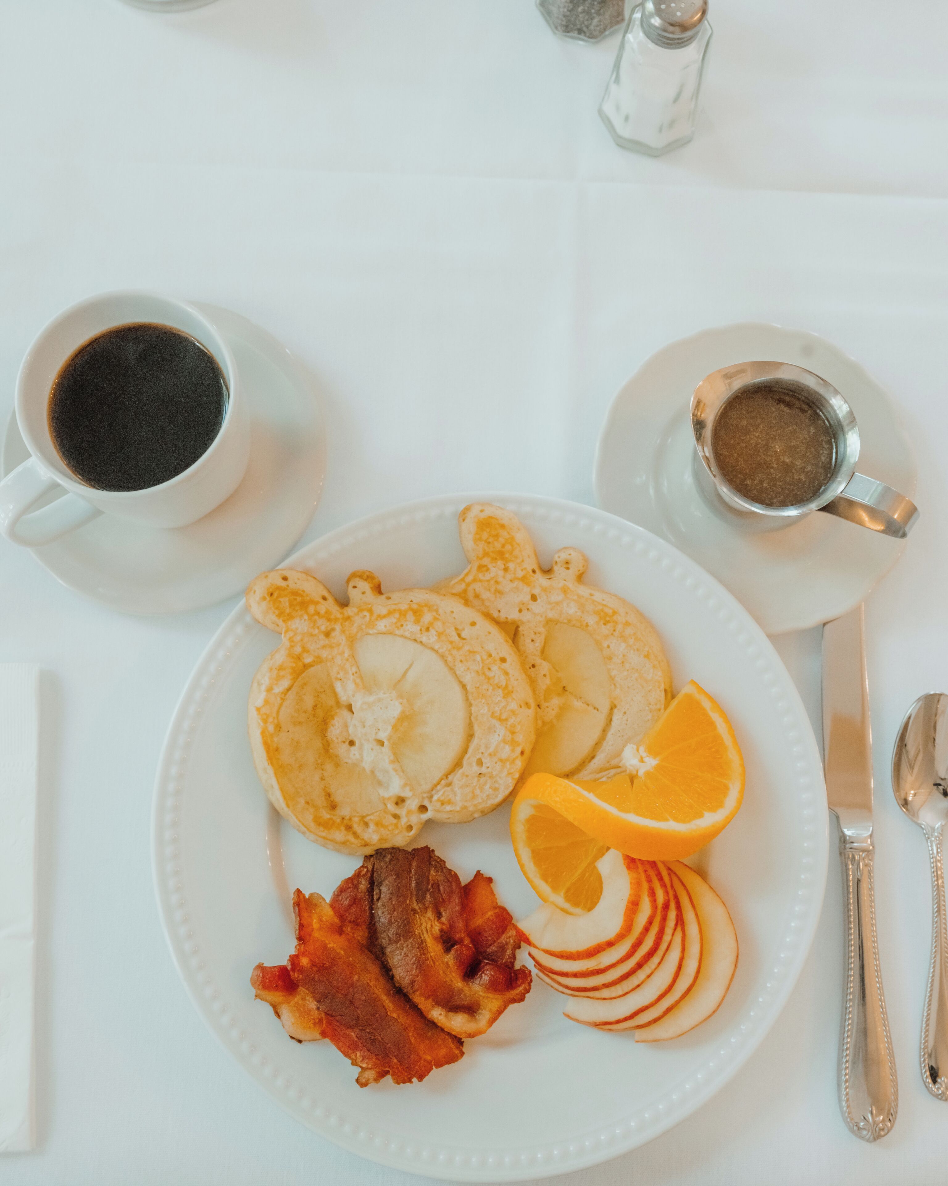 A breakfast plate with pancakes, bacon, apple slices, and orange segments.