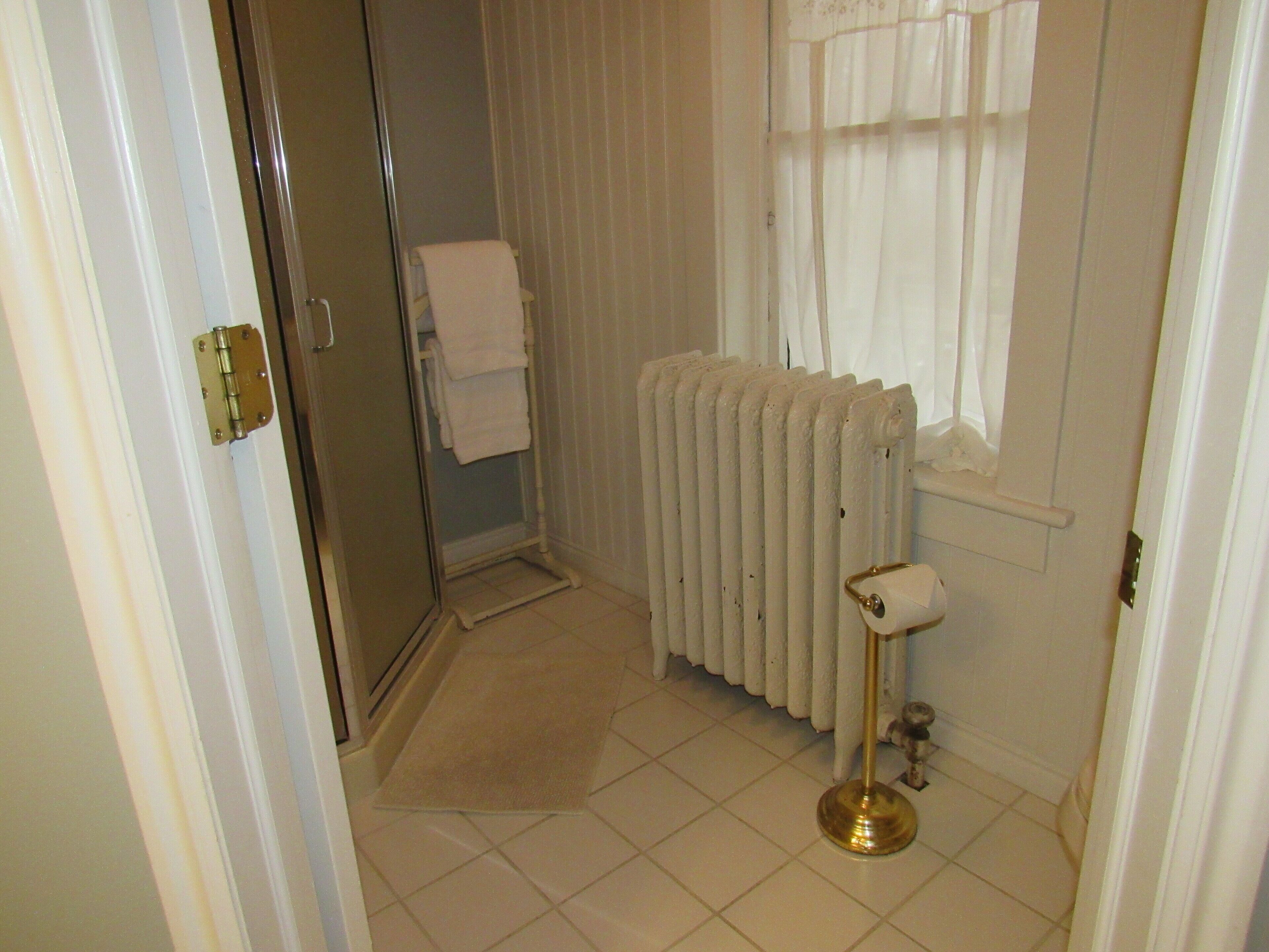 Un baño con un radiador blanco, un perchero y una puerta de ducha.