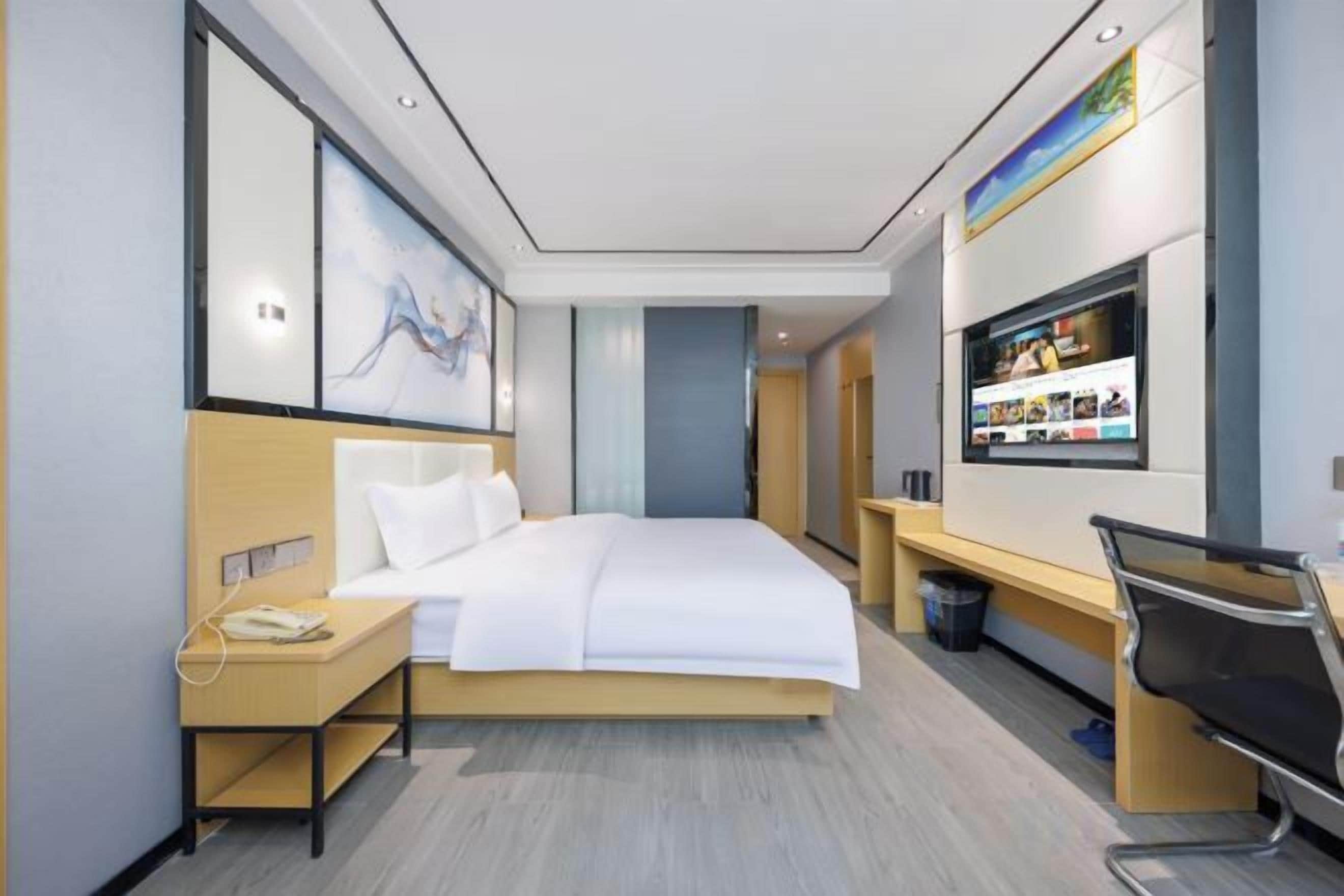 A hotel room with a bed, bedside table, desk, chair, and a wall-mounted TV.