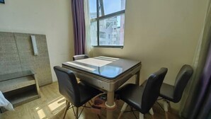 Un pequeño comedor con una mesa de vidrio, cuatro sillas negras, un banco de madera y una ventana con vistas a edificios.