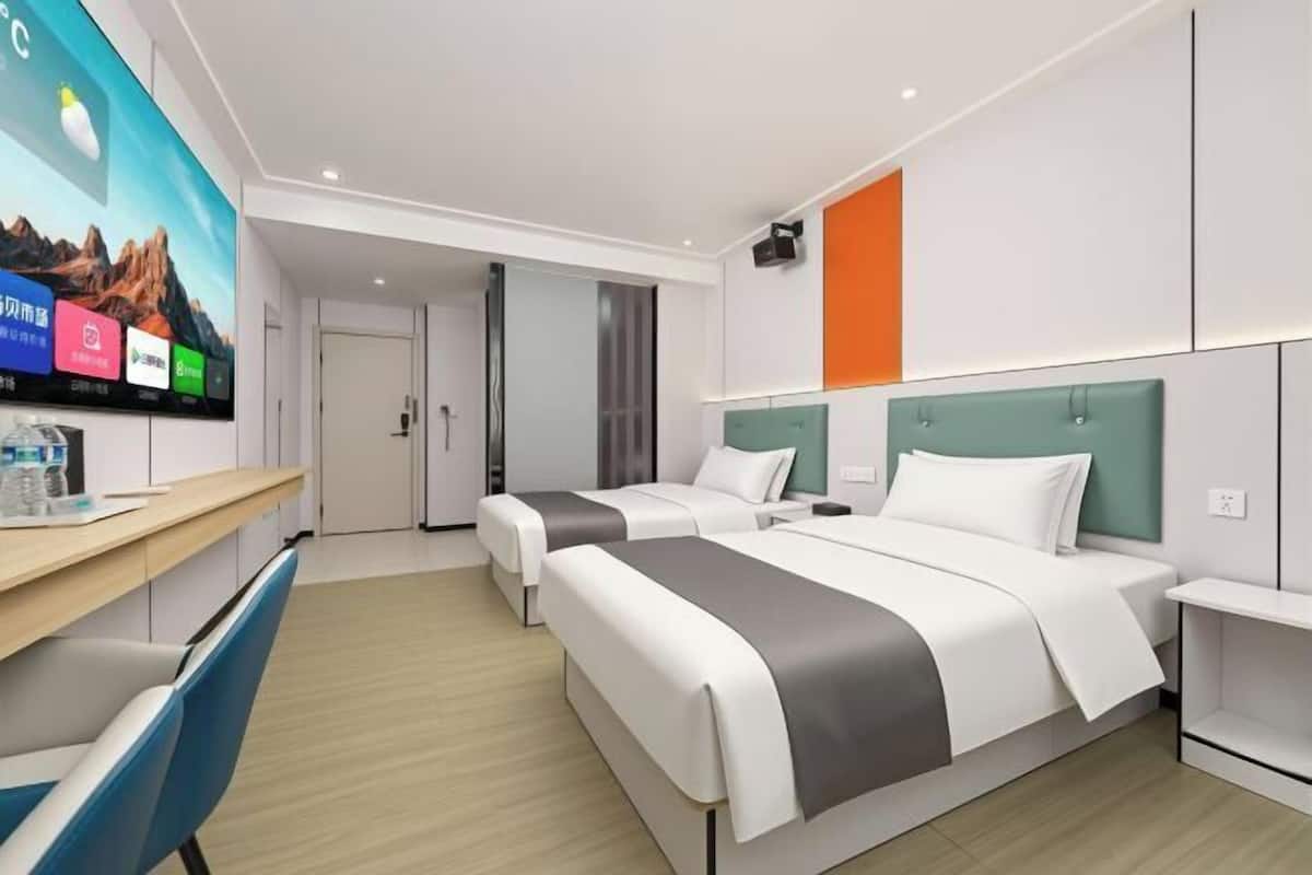 A hotel room with two beds, a desk, and a TV displaying a mountain landscape.