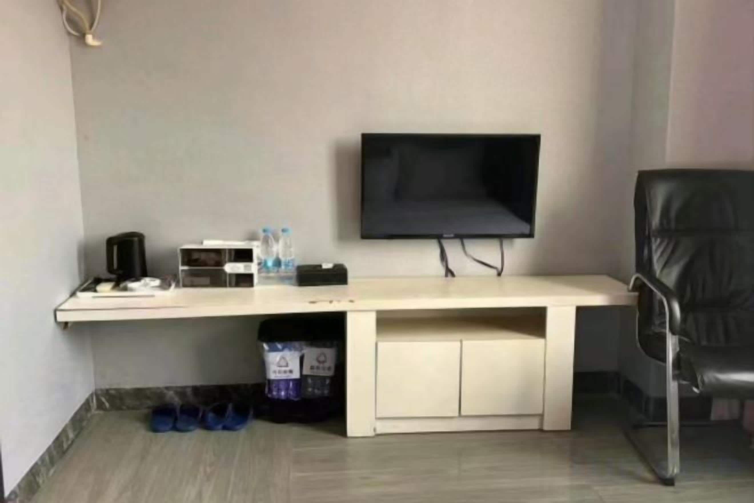 A room with a desk, a television mounted on the wall, a chair, and a storage unit under the desk.