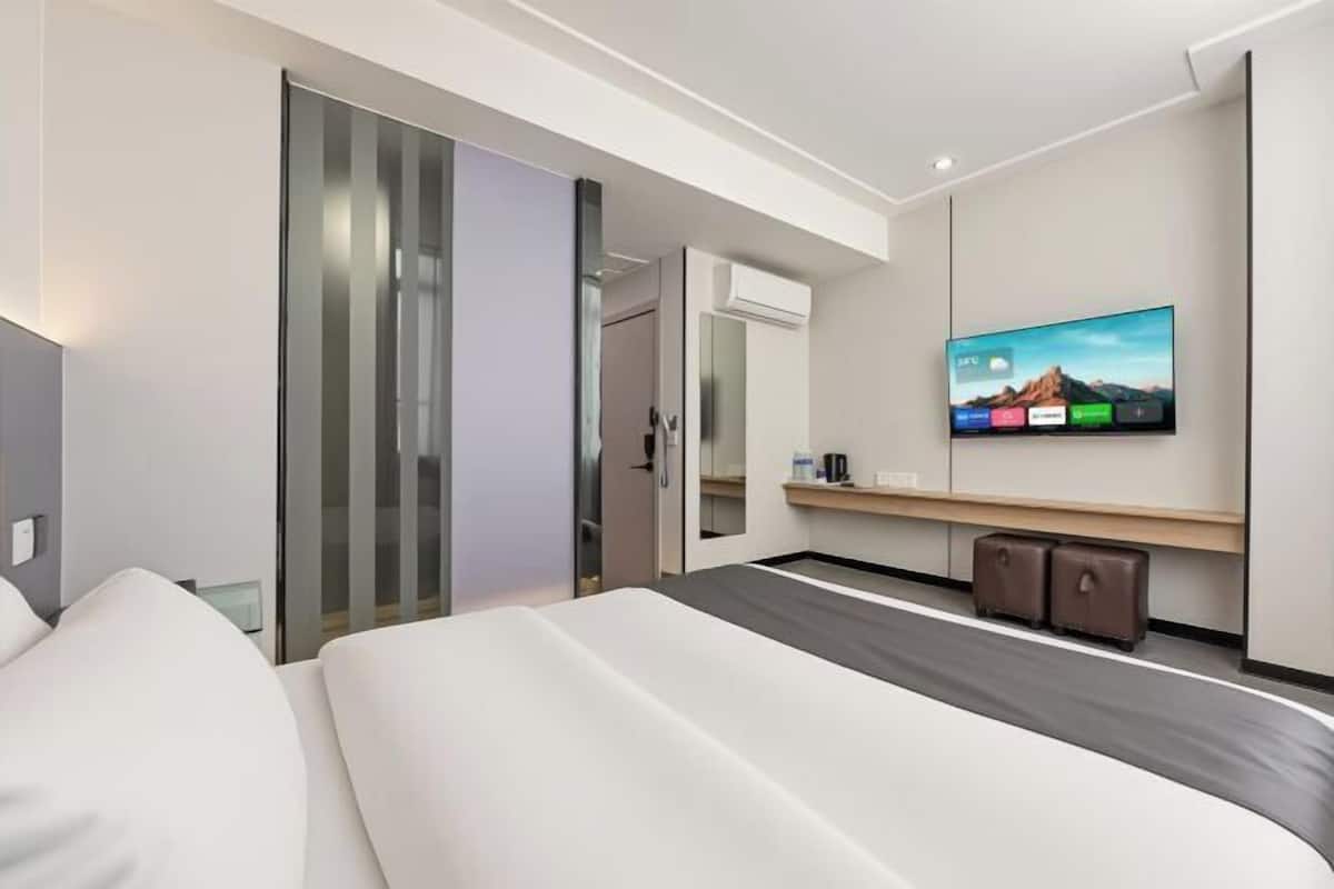 A modern hotel room with a bed, a flat-screen TV, a desk, and a mirror.