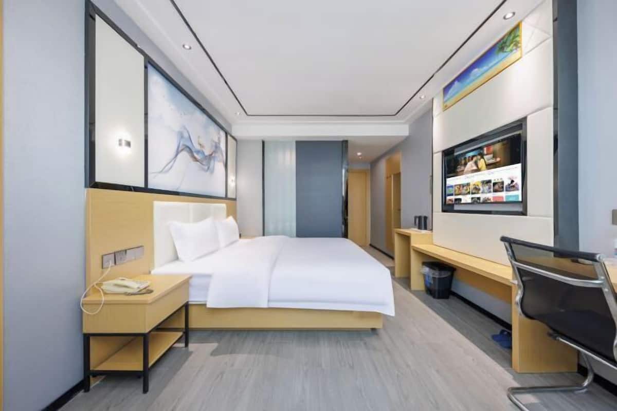 A modern hotel room with a bed, bedside table, chair, and a wall-mounted TV.