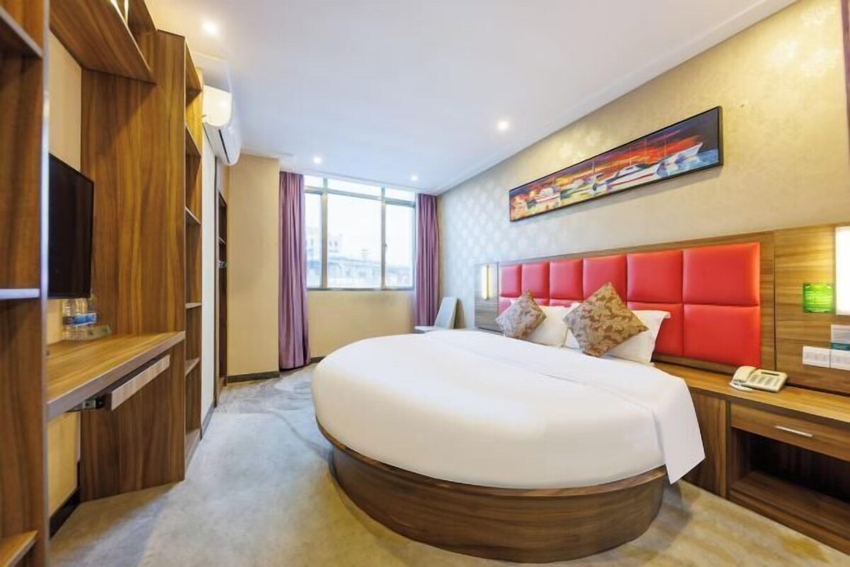 A hotel room with a large bed, wooden furniture, a painting on the wall, and a window with curtains.