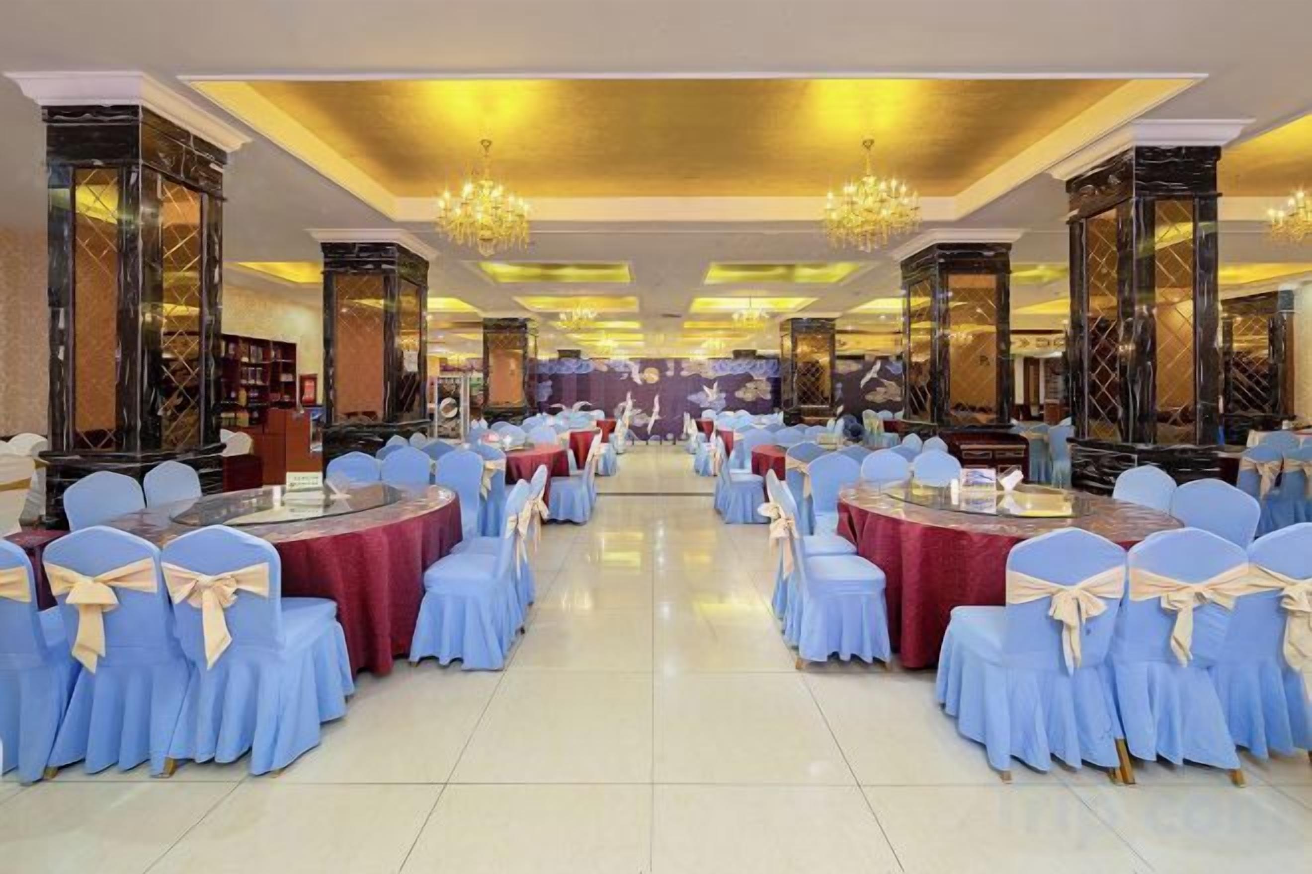 Une salle de banquet avec des tables rondes et des chaises, des lustres et des colonnes richement décorées.