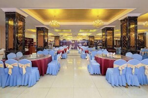 Un salón de banquetes con mesas redondas y sillas, candelabros y columnas decoradas.