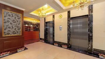 A hotel lobby with a reception desk, elevators, and a chandelier.