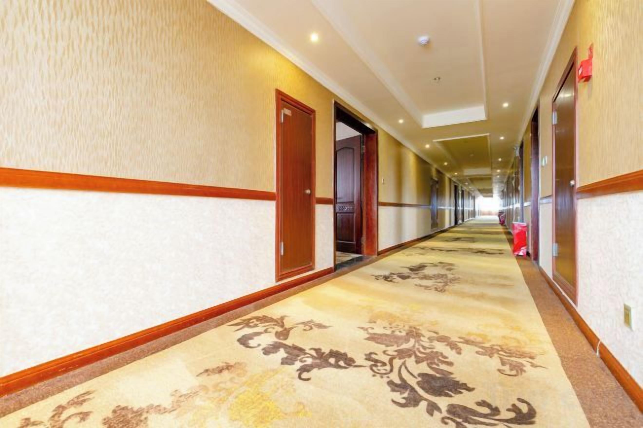 Un couloir d'hôtel avec un revêtement de sol en moquette, des portes en bois et un tapis de couloir à motifs.