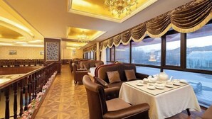 A restaurant with a long dining table, leather chairs, chandeliers, and large windows with a view. - Lia Daocheng Resort (Daocheng County)