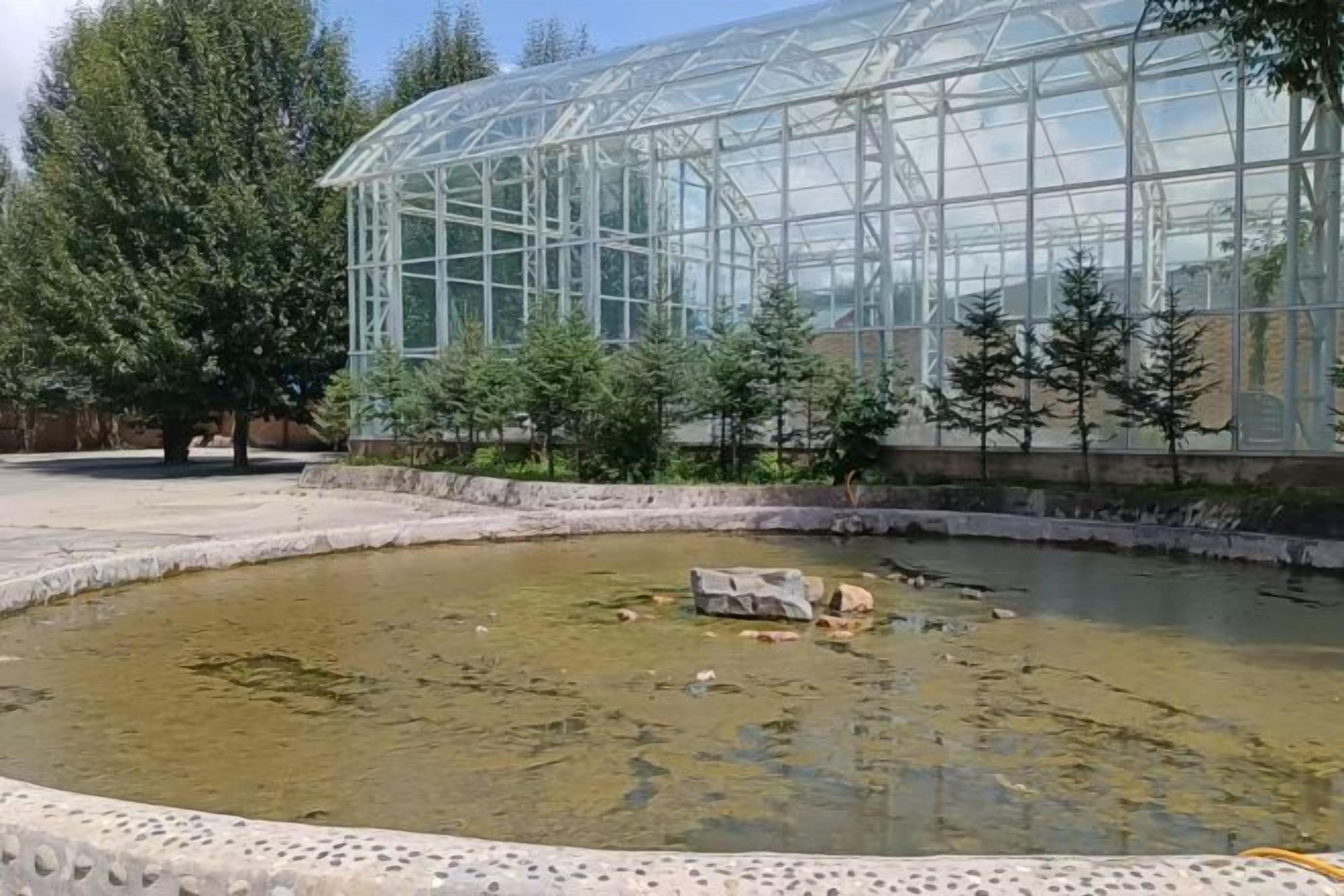 Una estructura invernadero con un estanque al frente.