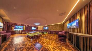 A spacious room with a billiards table, comfortable seating, and a large screen.