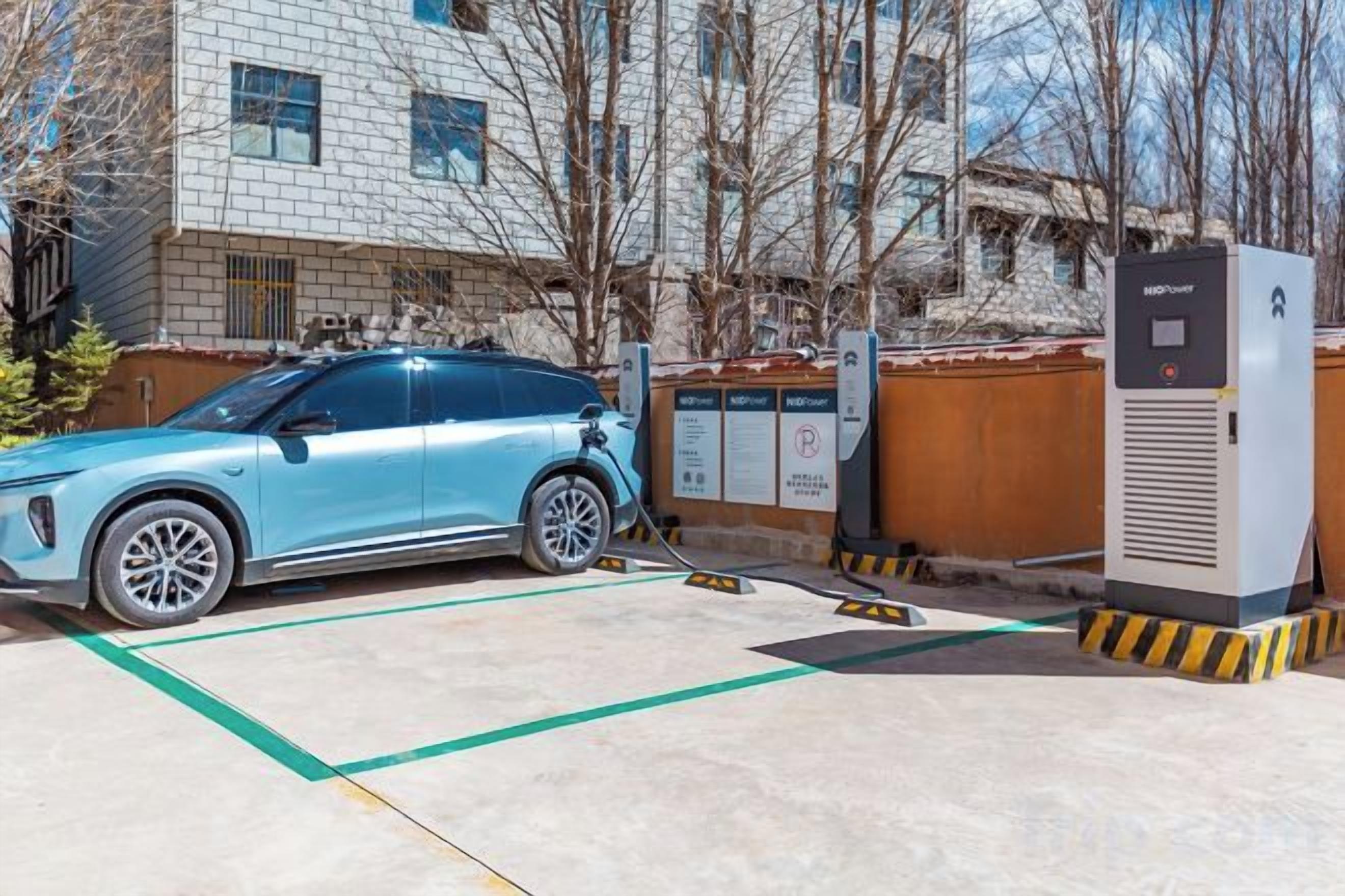 A light blue electric vehicle charging station in a parking lot with a building in the background.