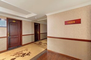 Pasillo de hotel con puertas de madera, piso alfombrado y un letrero que indica la dirección a la recepción.