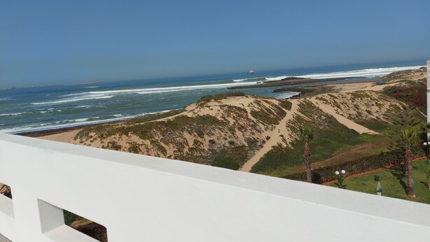 A coastal landscape with a sandy beach, dunes, and ocean waves. - Waterfront apartment (Mohammédia)