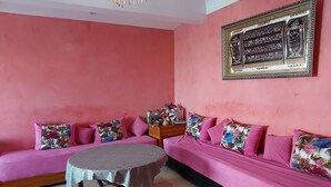 A room with a pink sofa set, a round table, and a decorative wall piece. - Waterfront apartment (Mohammédia)