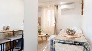Et moderne, lyst værelse med en seng, et lille bord med en plante og en stol.