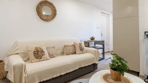 En stue med en beige sofa, et rundt spejl og en potteplante.