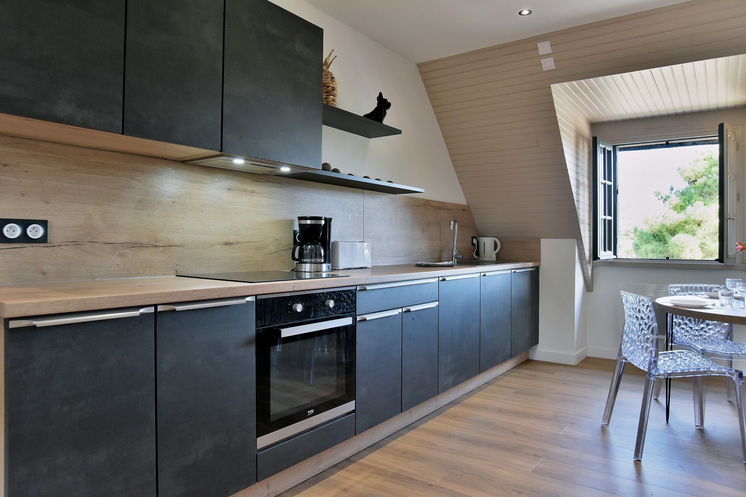 A modern kitchen with dark cabinets, a built-in oven, and a coffee maker.