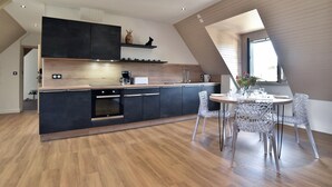 Una cocina moderna con armarios oscuros, encimera de madera y una zona de comedor con sillas transparentes.
