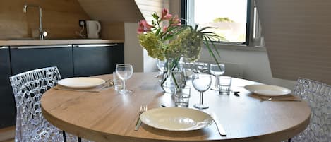 A dining table set with plates, cutlery, and glasses, surrounded by clear chairs, in a room with a wooden ceiling and a window.