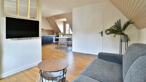 Una sala de estar moderna con un sofá gris, una mesa de centro redonda de madera y un televisor de pantalla plana montado en la pared.