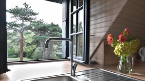 A kitchen with a stainless steel sink, a window with a view of trees, and a vase with flowers on the counter.