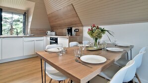 A modern kitchen with white cabinets, a wooden dining table set for four, and a coffee machine.