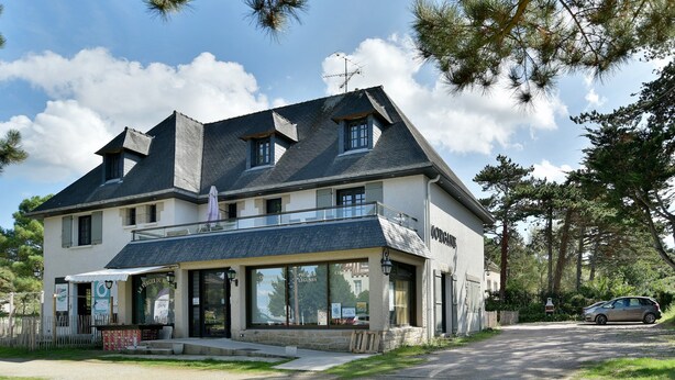 A two-story building with a balcony, large windows, and a gravel driveway.