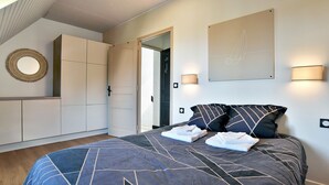 A bedroom with a large bed, a wardrobe, a mirror, and two wall-mounted lights.