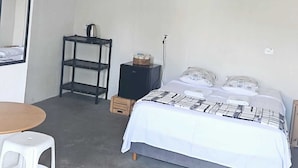 A bedroom with a bed, a small table, a chair, a shelf, and a kettle.