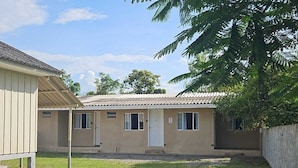 A single-story building with a flat roof, a covered porch, and a small front yard with grass and a concrete wall.