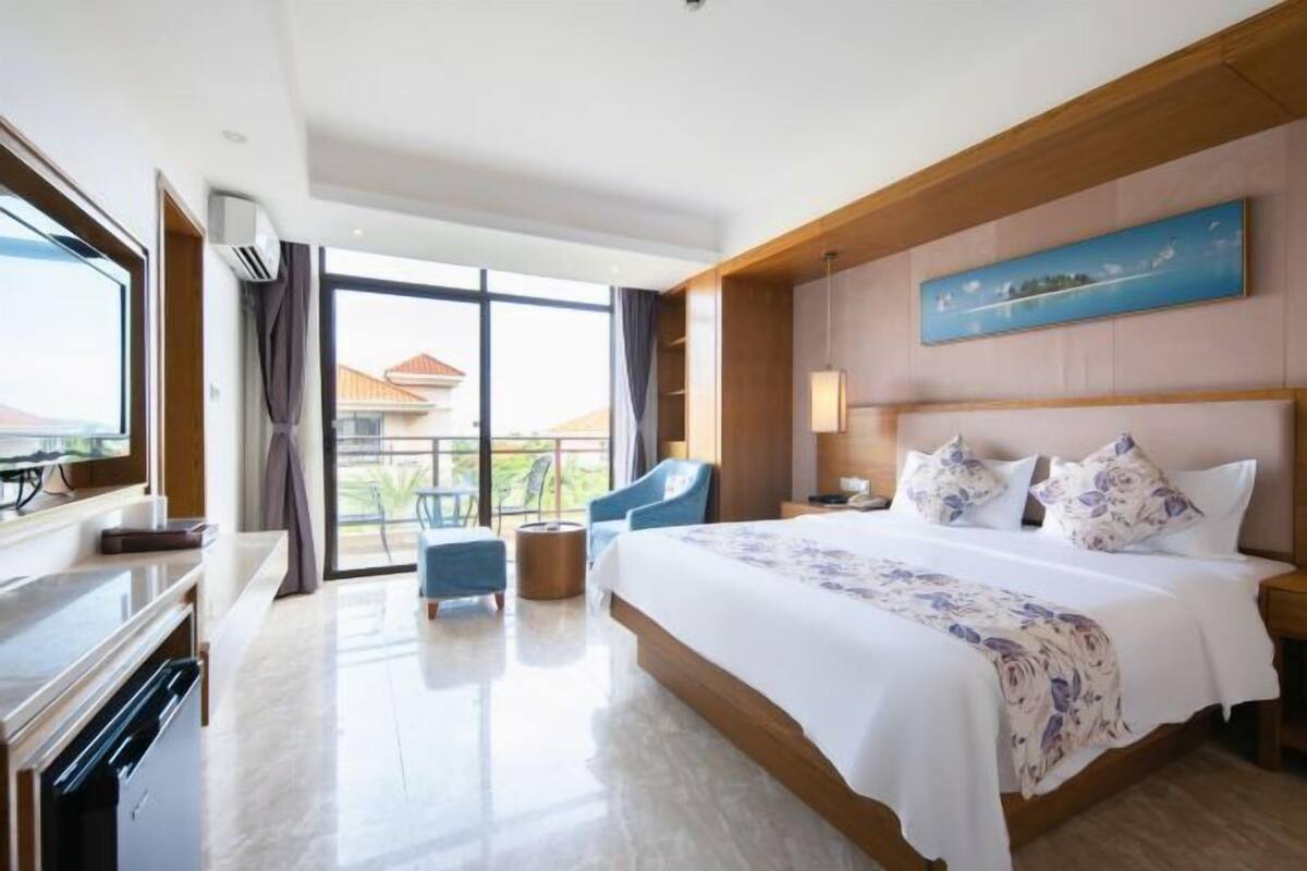 Quarto de hotel moderno com cama grande, escrivaninha, cadeira e vista para a varanda.