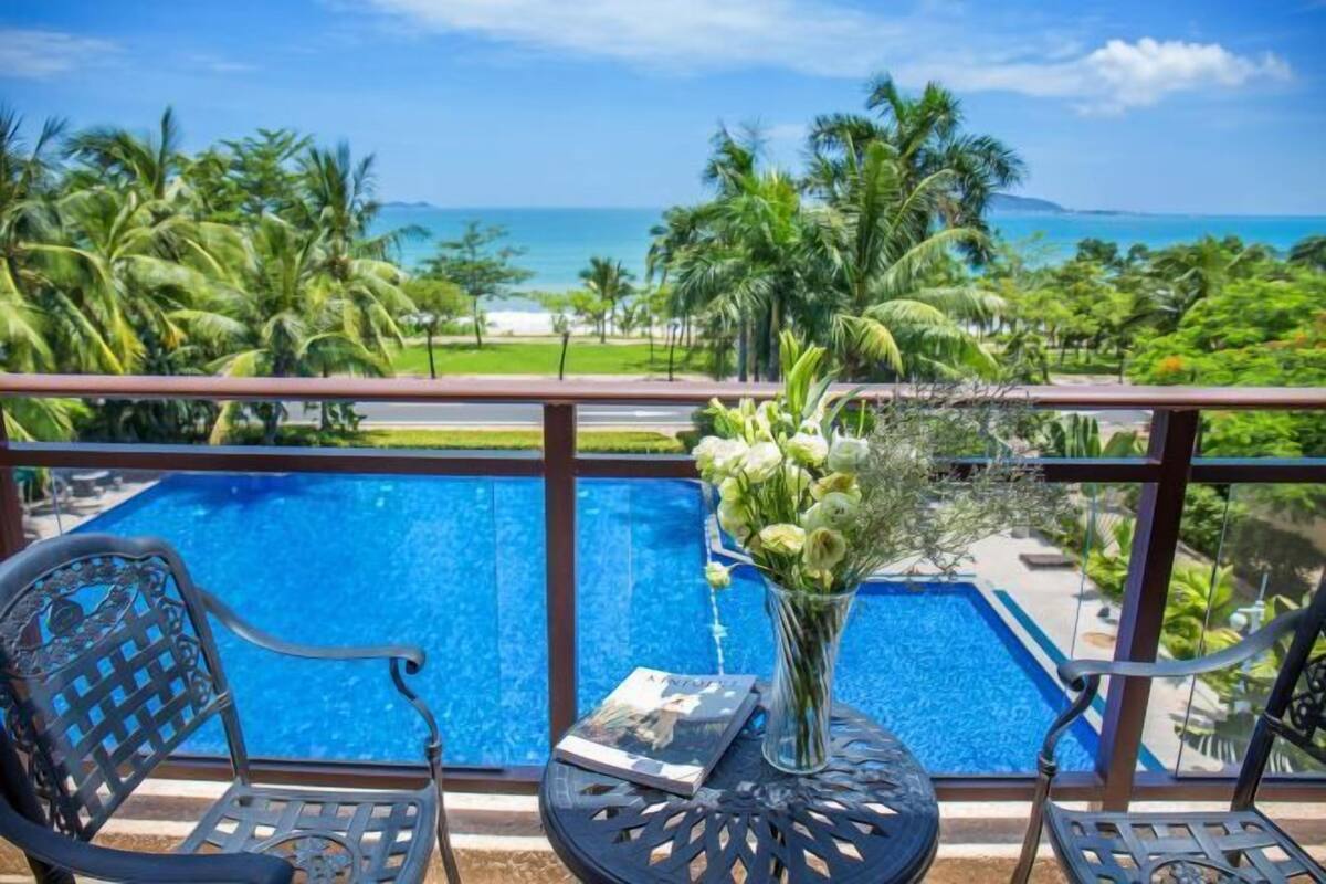 Uma varanda com vista para uma piscina, palmeiras e o oceano.