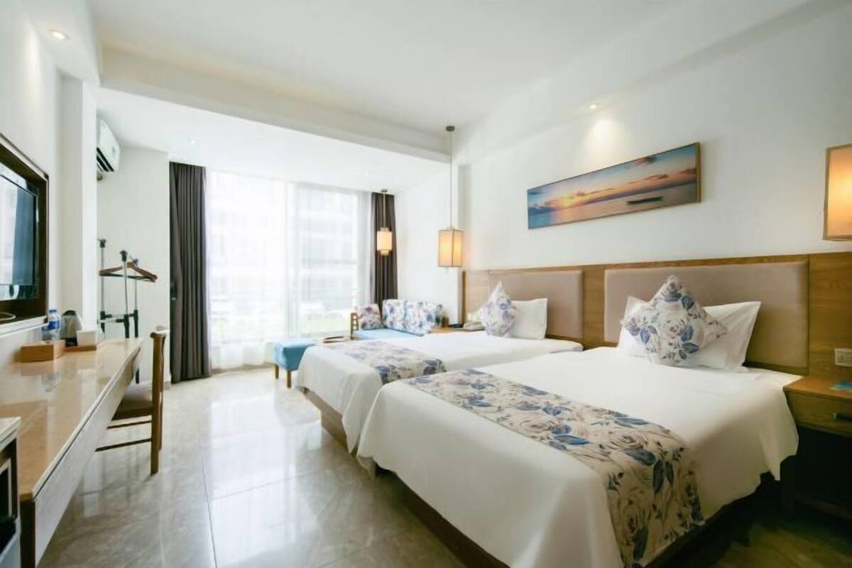 Quarto de hotel com duas camas, uma mesa e vista para a cidade.