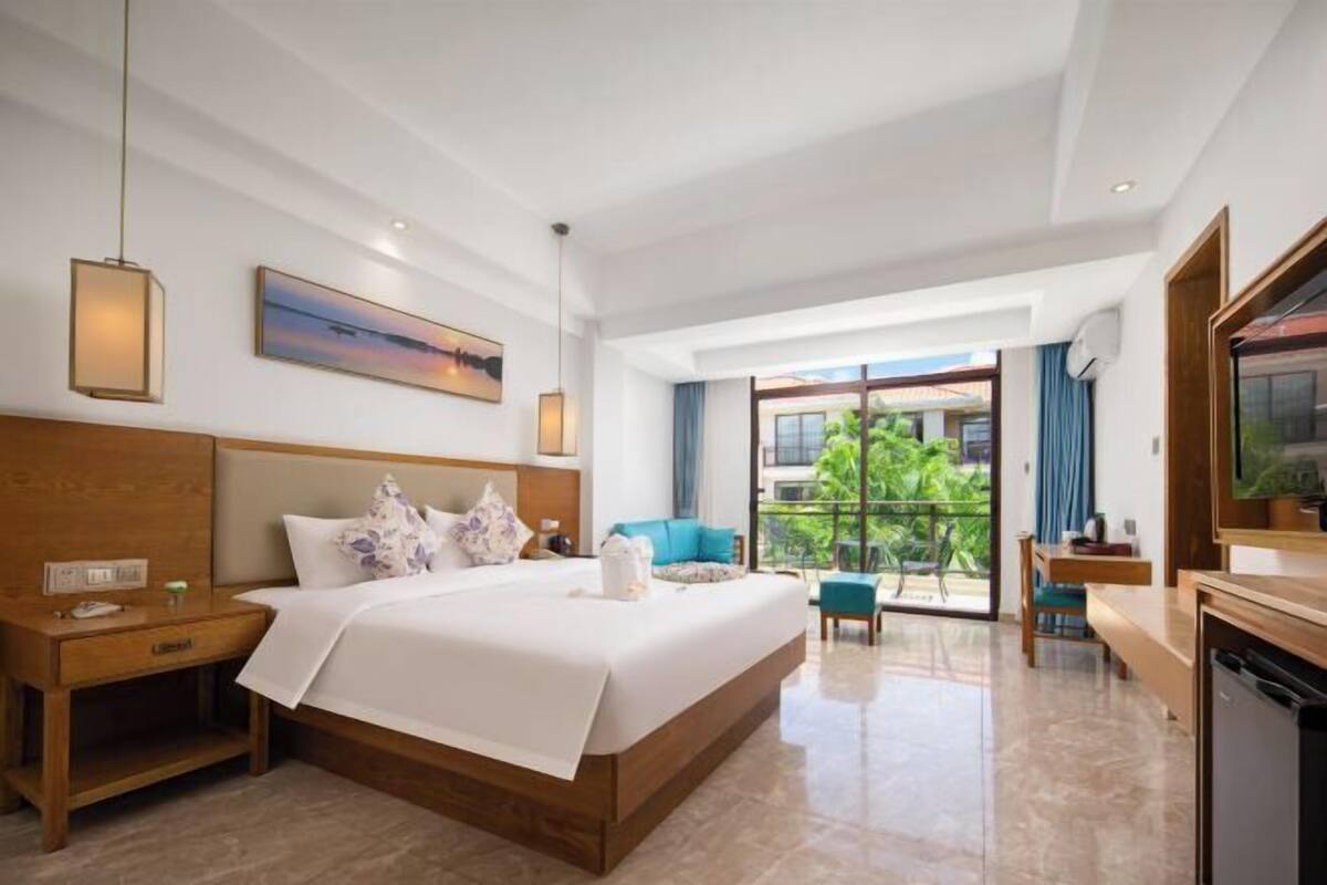 Quarto de hotel com uma cama grande, escrivaninha, cadeira, televisão e varanda com vista.