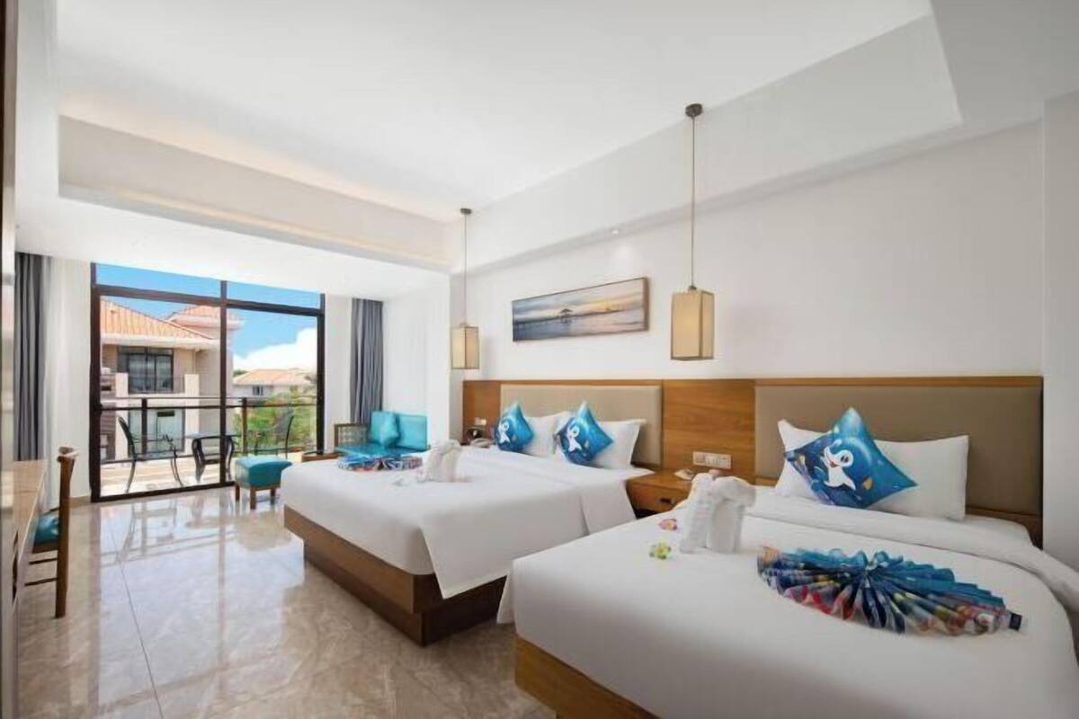 Quarto de hotel com duas camas, varanda, área de refeições e vista para o exterior.