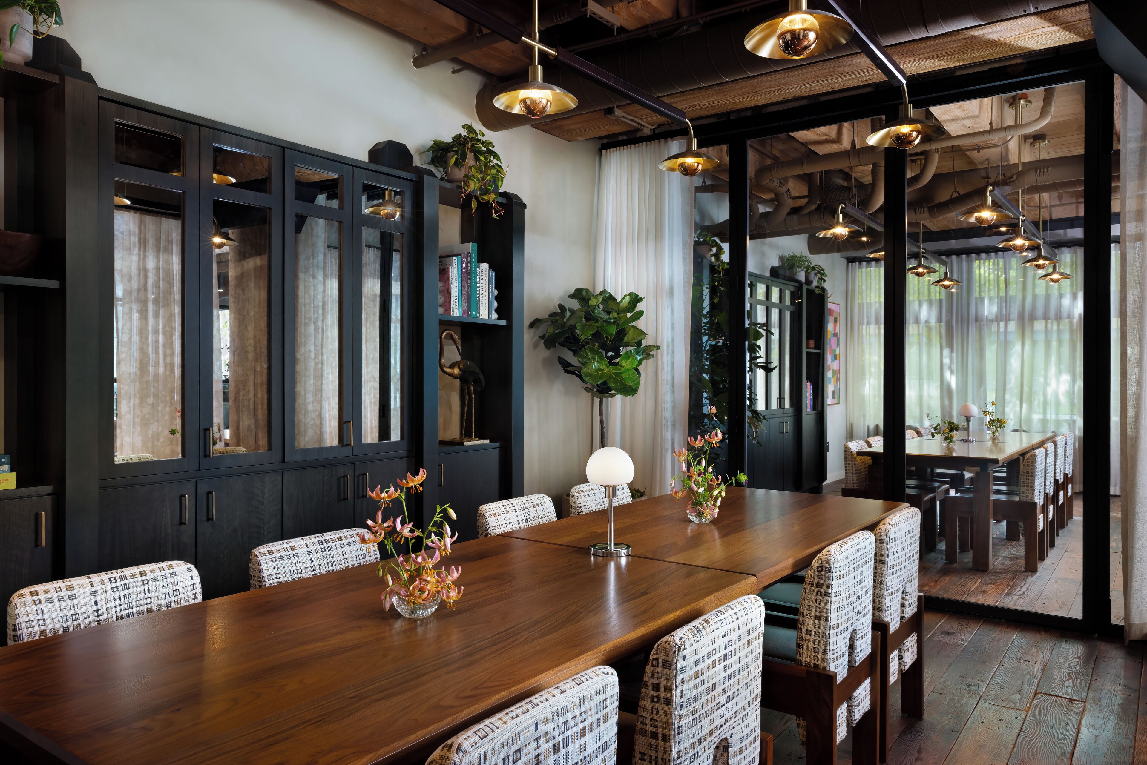 A dining area with a long wooden table, patterned chairs, and hanging pendant lights.