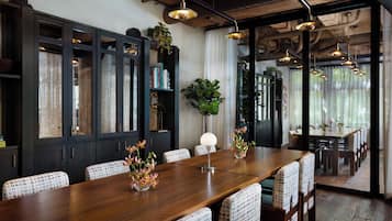 A dining area with a long wooden table, patterned chairs, and hanging pendant lights.