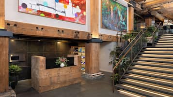 A modern lobby with a wooden reception desk, a staircase, and large abstract paintings on the walls.