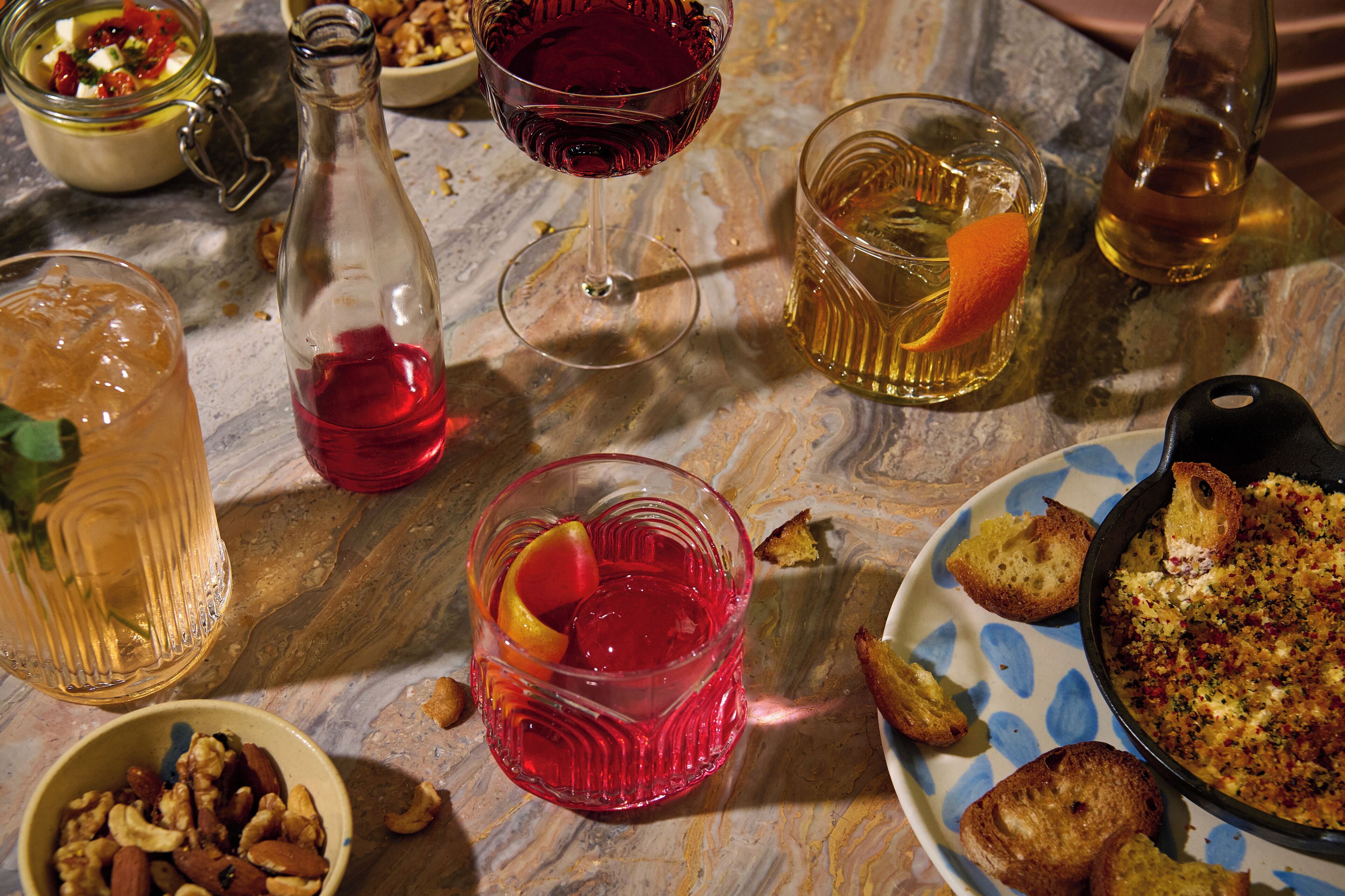 Una mesa con diversas bebidas, un bol de frutos secos y un plato de pan.