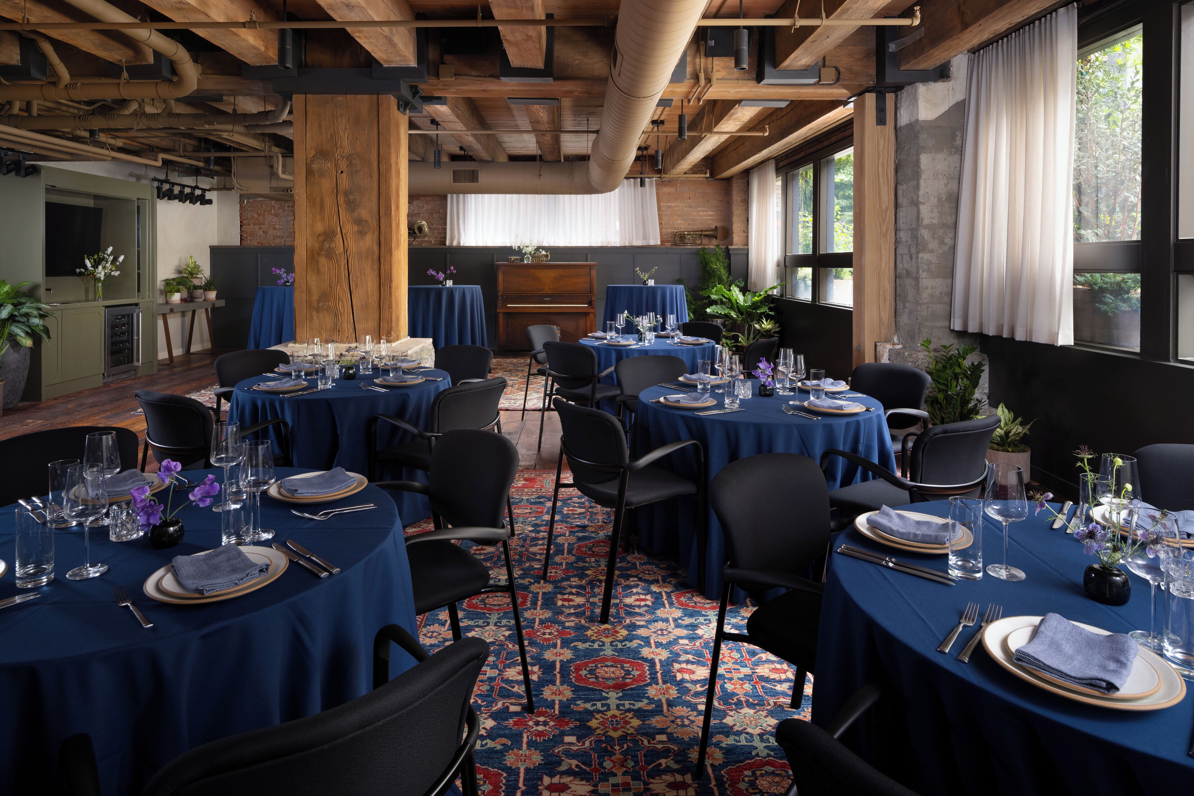 A dining area with round tables set for a meal, featuring blue tablecloths and a patterned carpet.