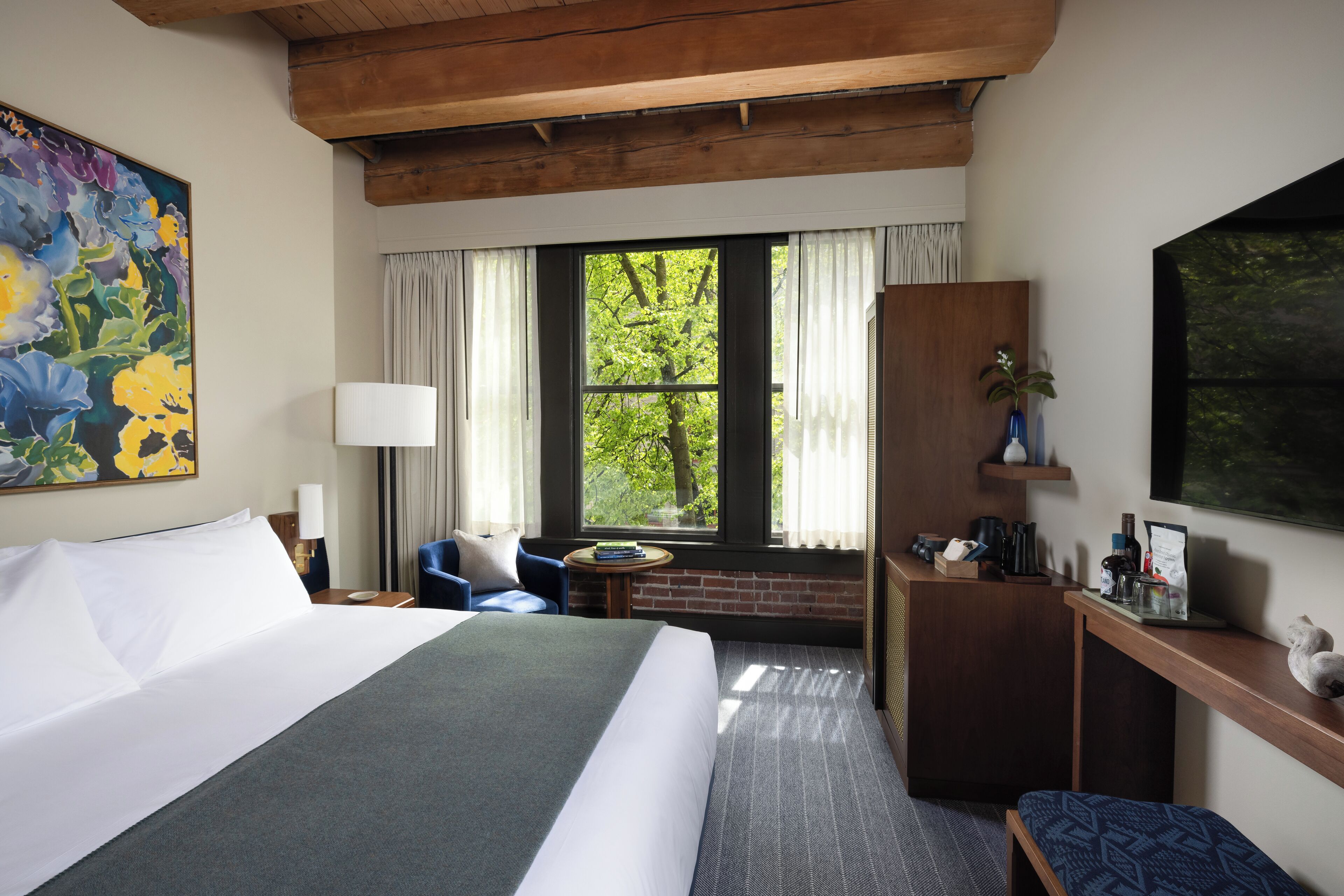 A hotel room with a large bed, a desk, a chair, a window with curtains, and a painting on the wall.
